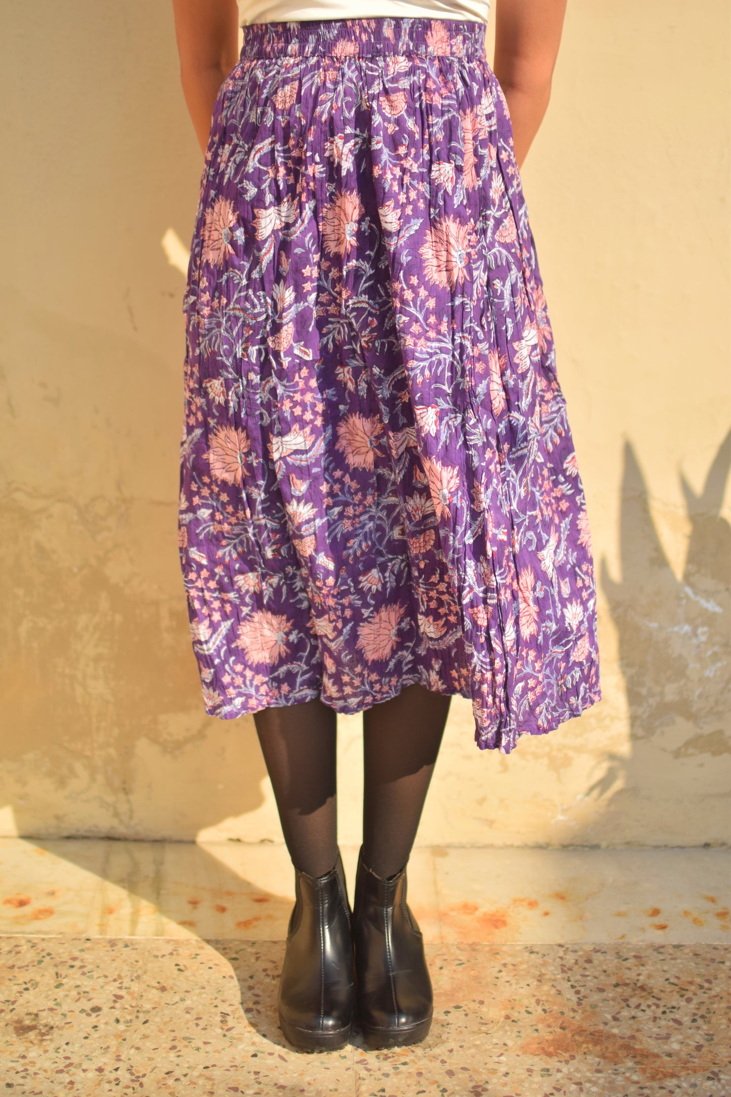 Person wearing a purple floral skirt with black shoes on a beige background