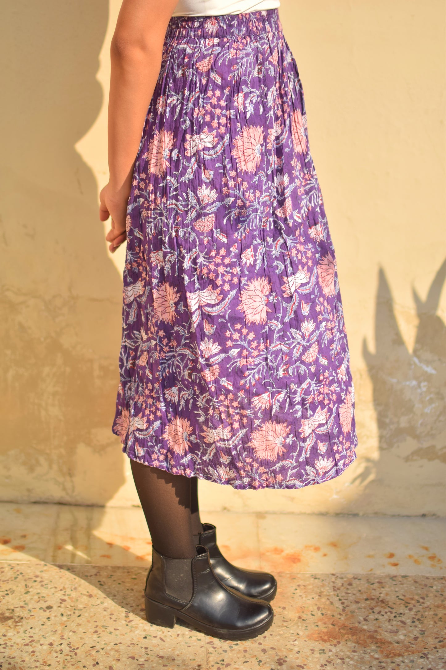 Person wearing a purple floral skirt with black boots on a beige background