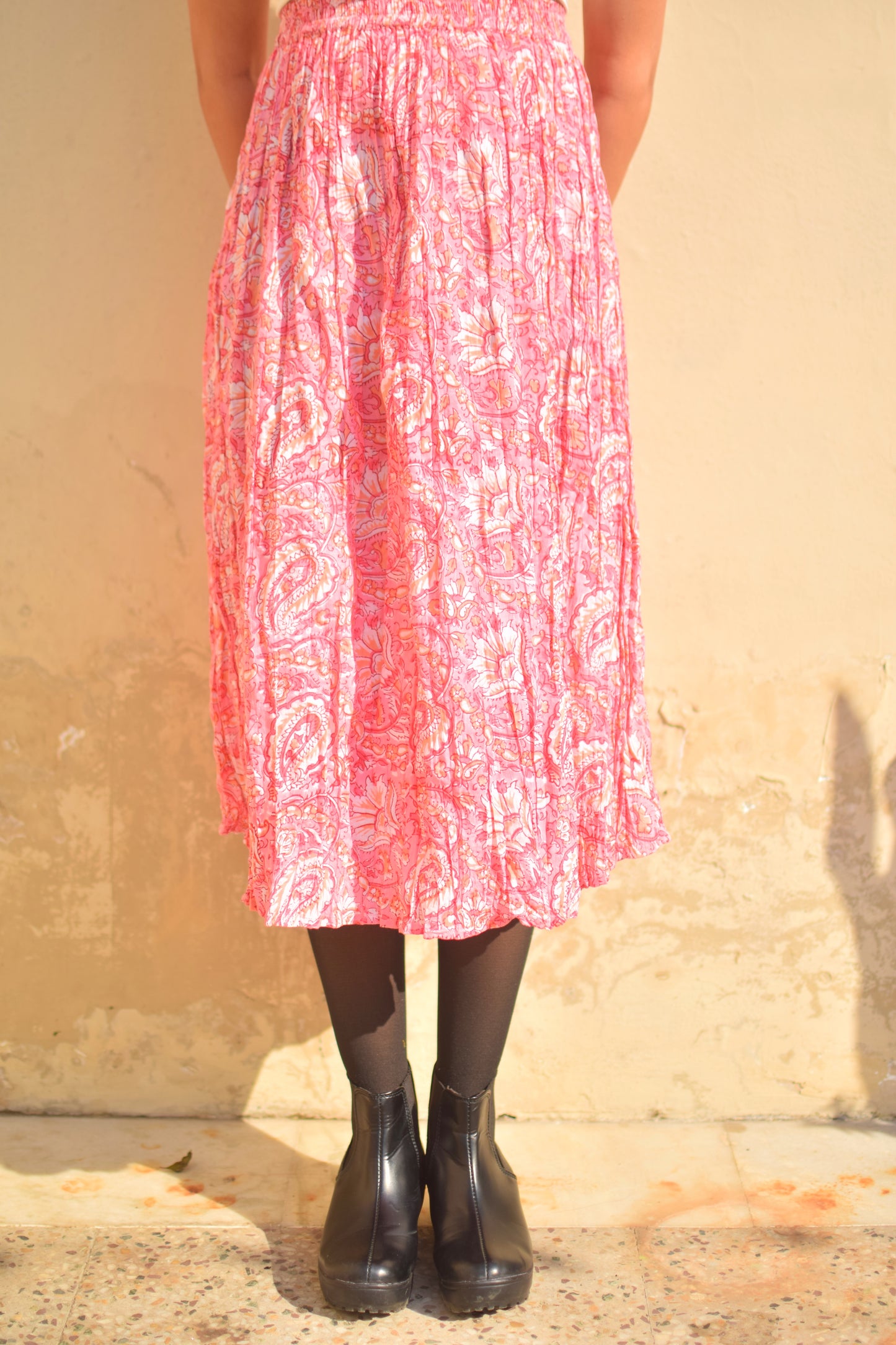 Person wearing a pink patterned dress and black boots against a beige wall.