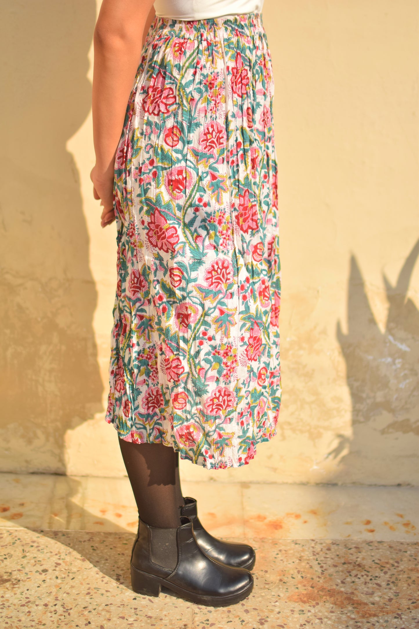 Person wearing a floral skirt and black boots against a beige wall.