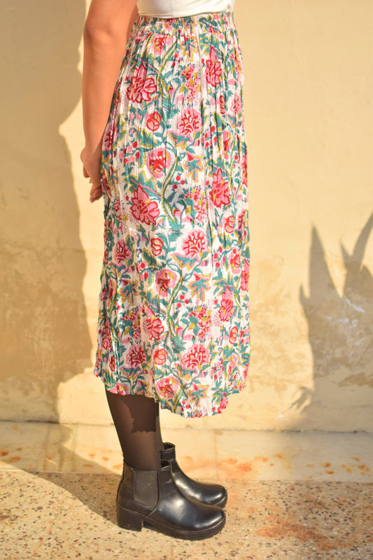 Person wearing a floral skirt and black boots against a beige wall.