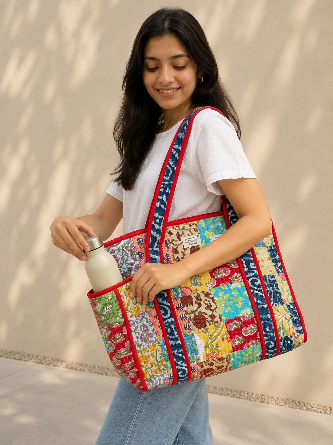 Woman holding a colorful patchwork quilted tote bag against a beige wall.