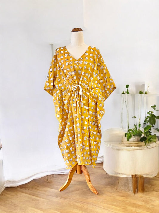 Yellow elephant hand block printed kaftan on a mannequin against a white wall with a small table and plants in the background.