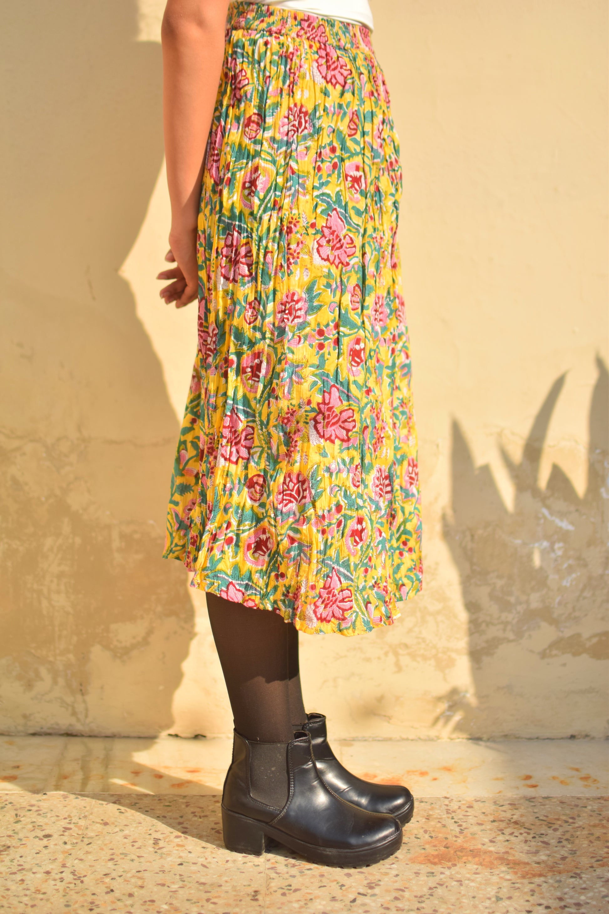 Person wearing a colorful floral skirt and black boots against a beige wall.