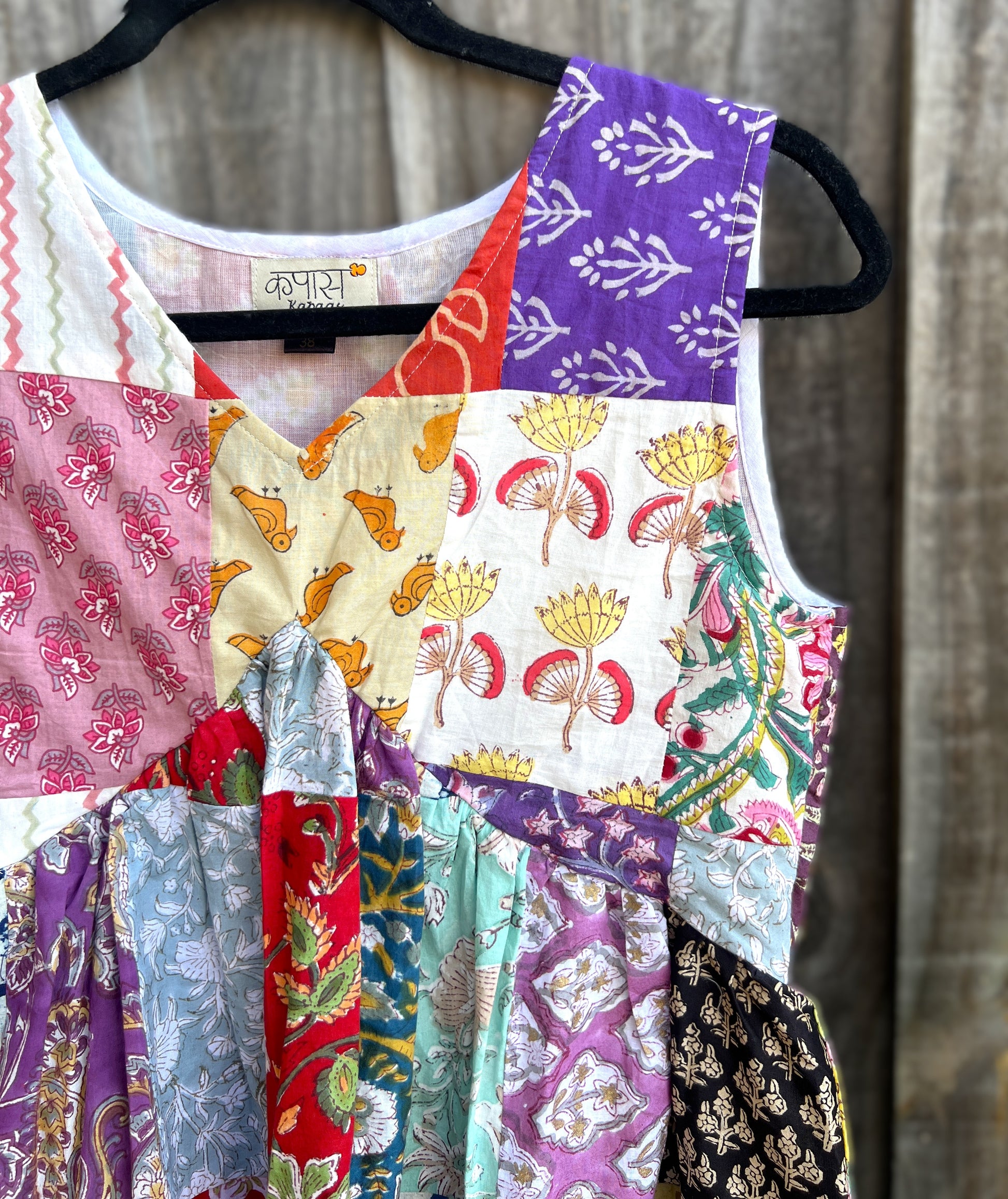 Colorful hand block patchwork top on a hanger against a wooden background