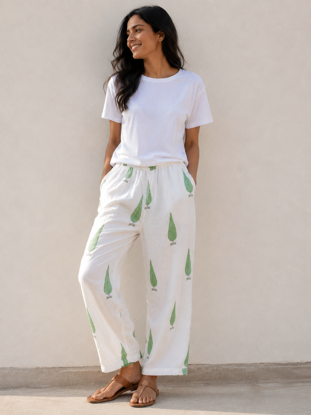 Woman wearing a white t-shirt and white sage cypress print pants standing against a beige wall.