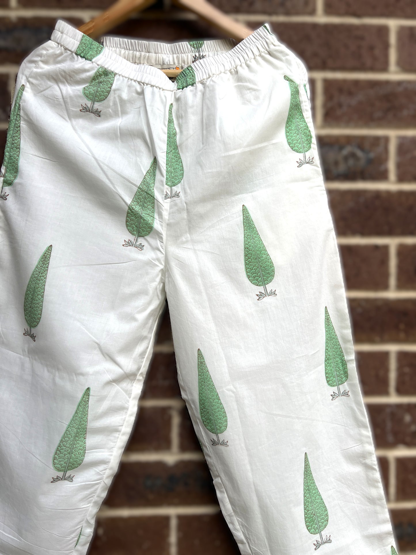 Close up of White sage cypress print pants hanging against a brick wall.