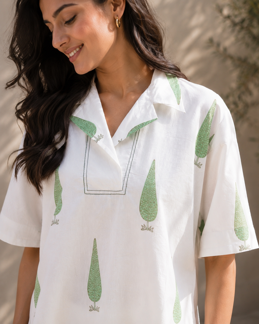 Woman smiling white wearing a white sage cypress print lounge shirt  against a neutral background