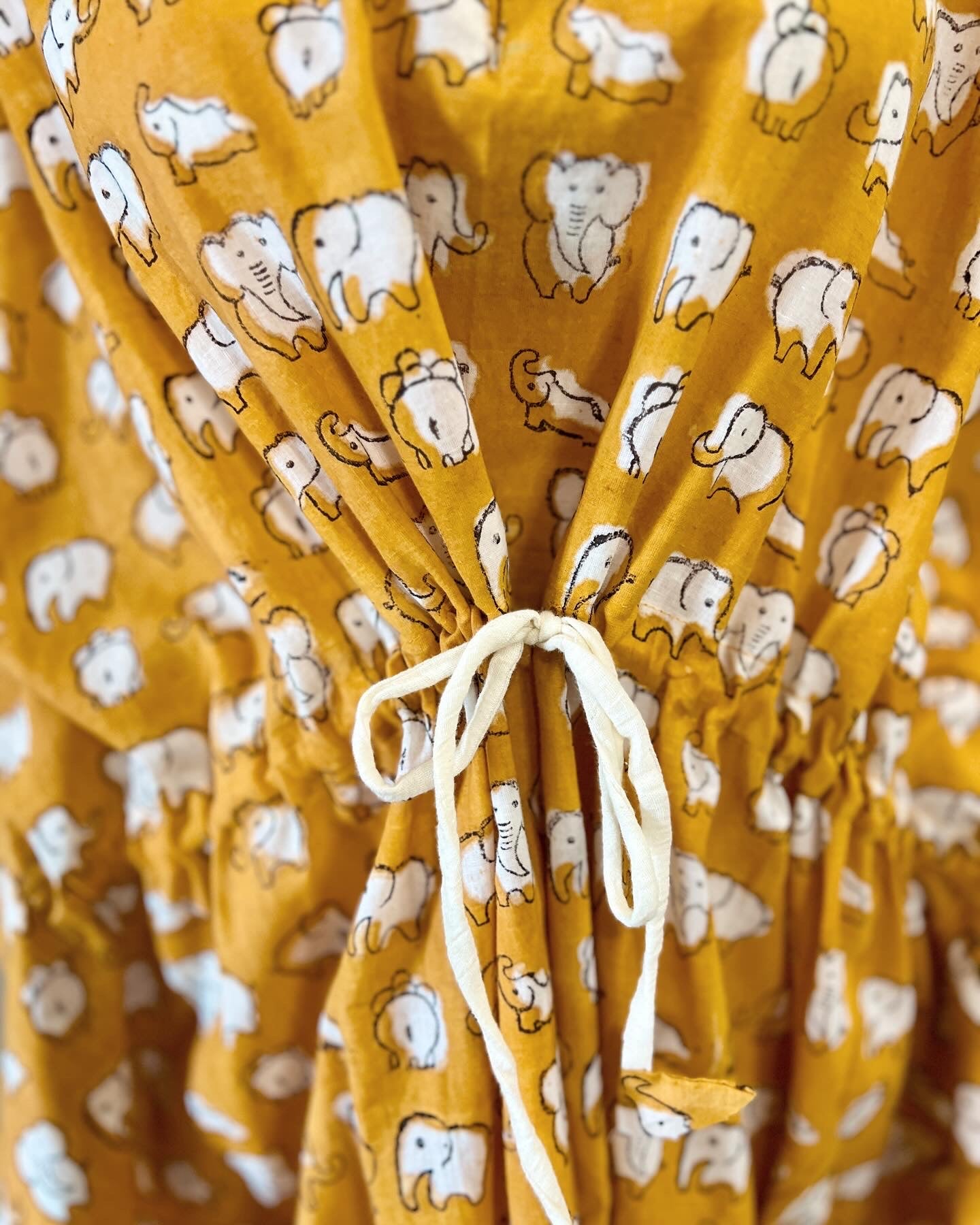 close up shot of a yellow elephant hand block printed kaftan on a mannequin against a white wall with a small table and plants in the background