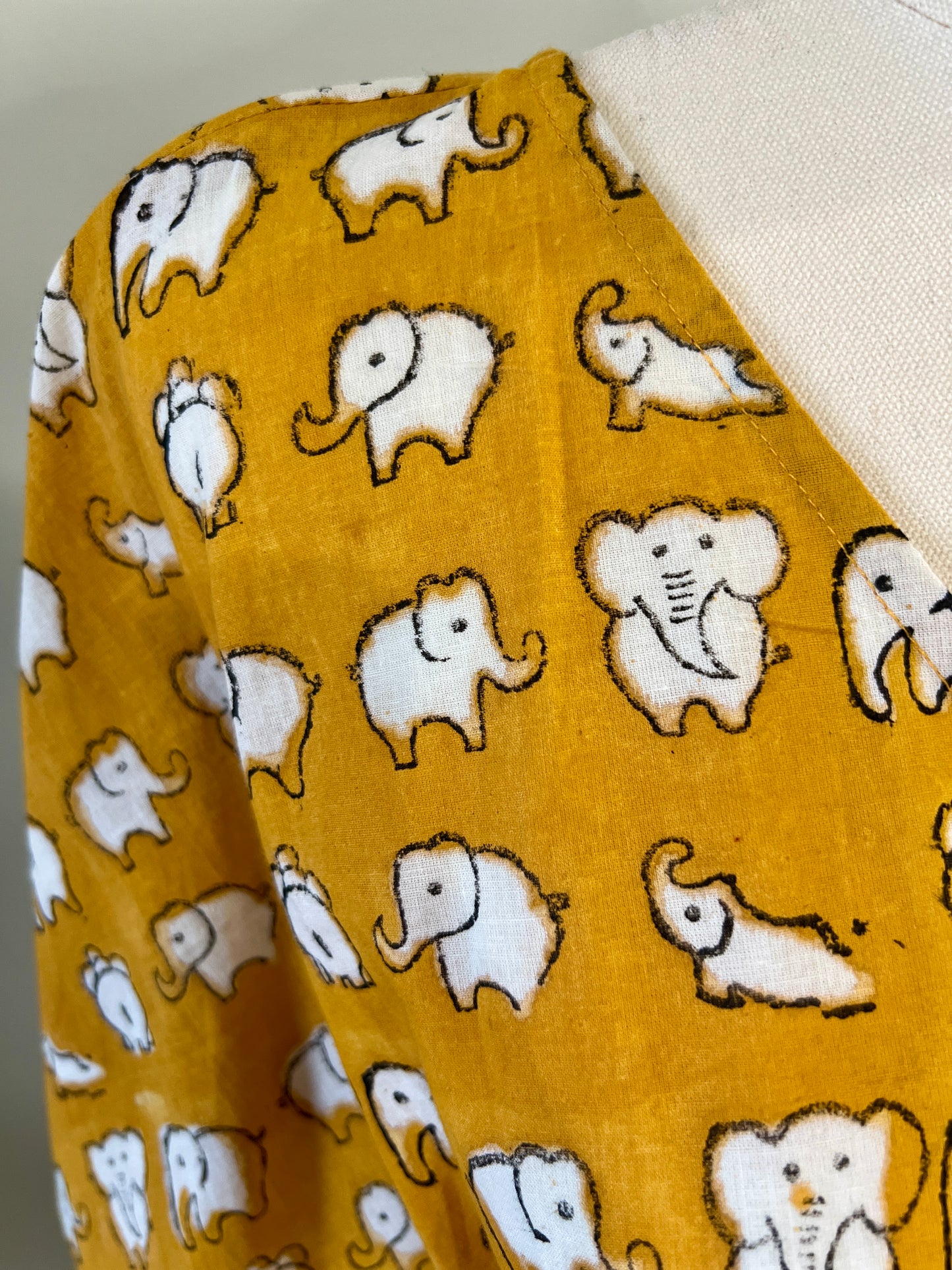 Close up shot of yellow elephant hand block printed kaftan on a mannequin against a white wall with a small table and plants in the background