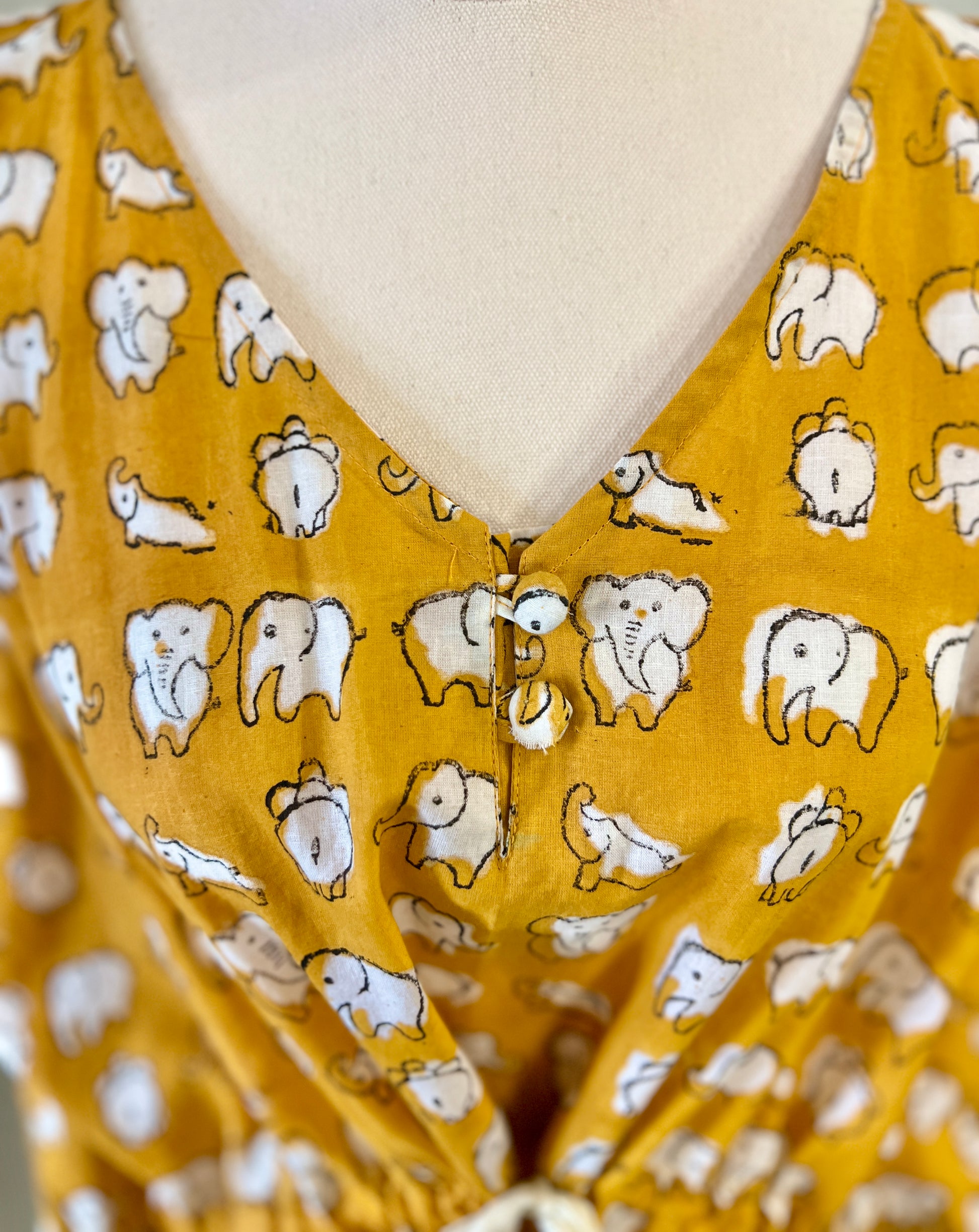 Neck style of yellow elephant hand block printed kaftan on a mannequin against a white wall with a small table and plants in the background